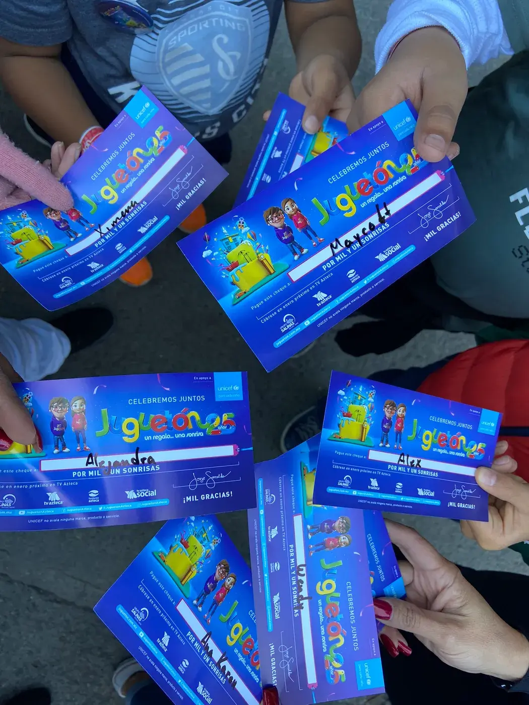 Manos infantiles sostienen cheques simbólicos de la campaña Juguetón Azteca