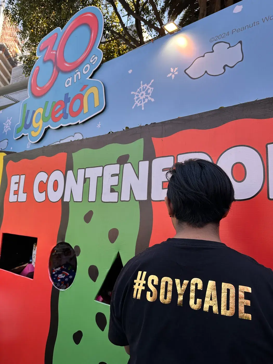 Integrante de CADE con playera #SOYCADE frente al contenedor de juguetes del Juguetón