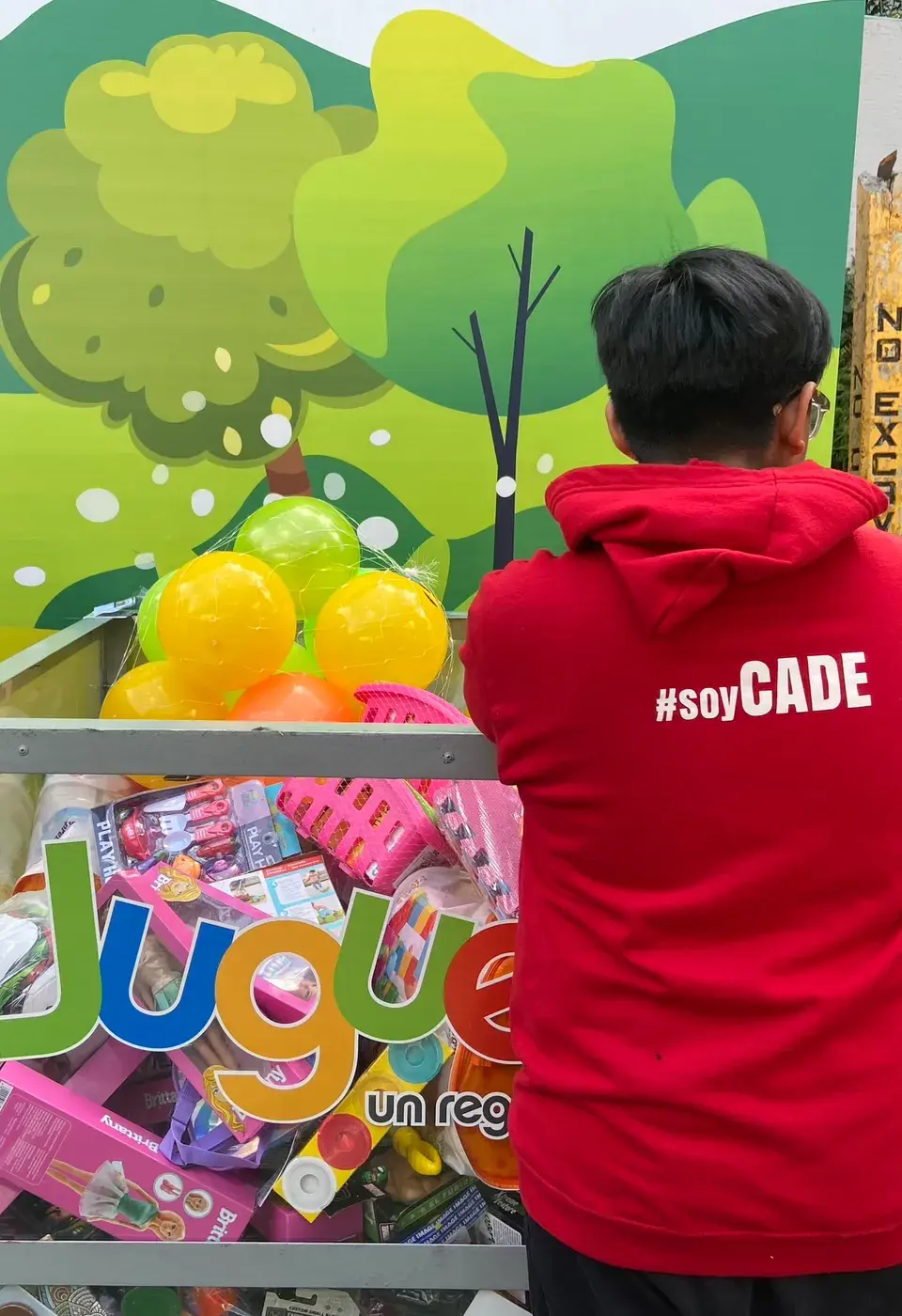 Joven de espaldas deposita juguetes en la colecta del Juguetón Azteca