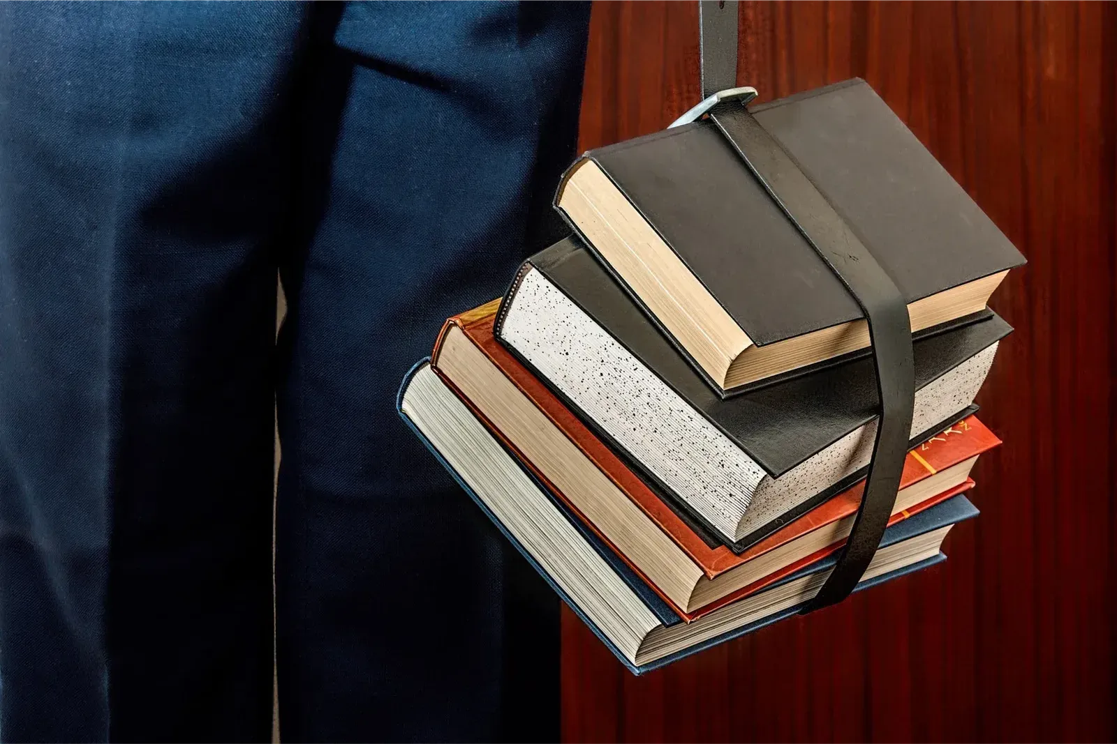 Persona con traje carga una pila de libros sujeta con una correa de piel