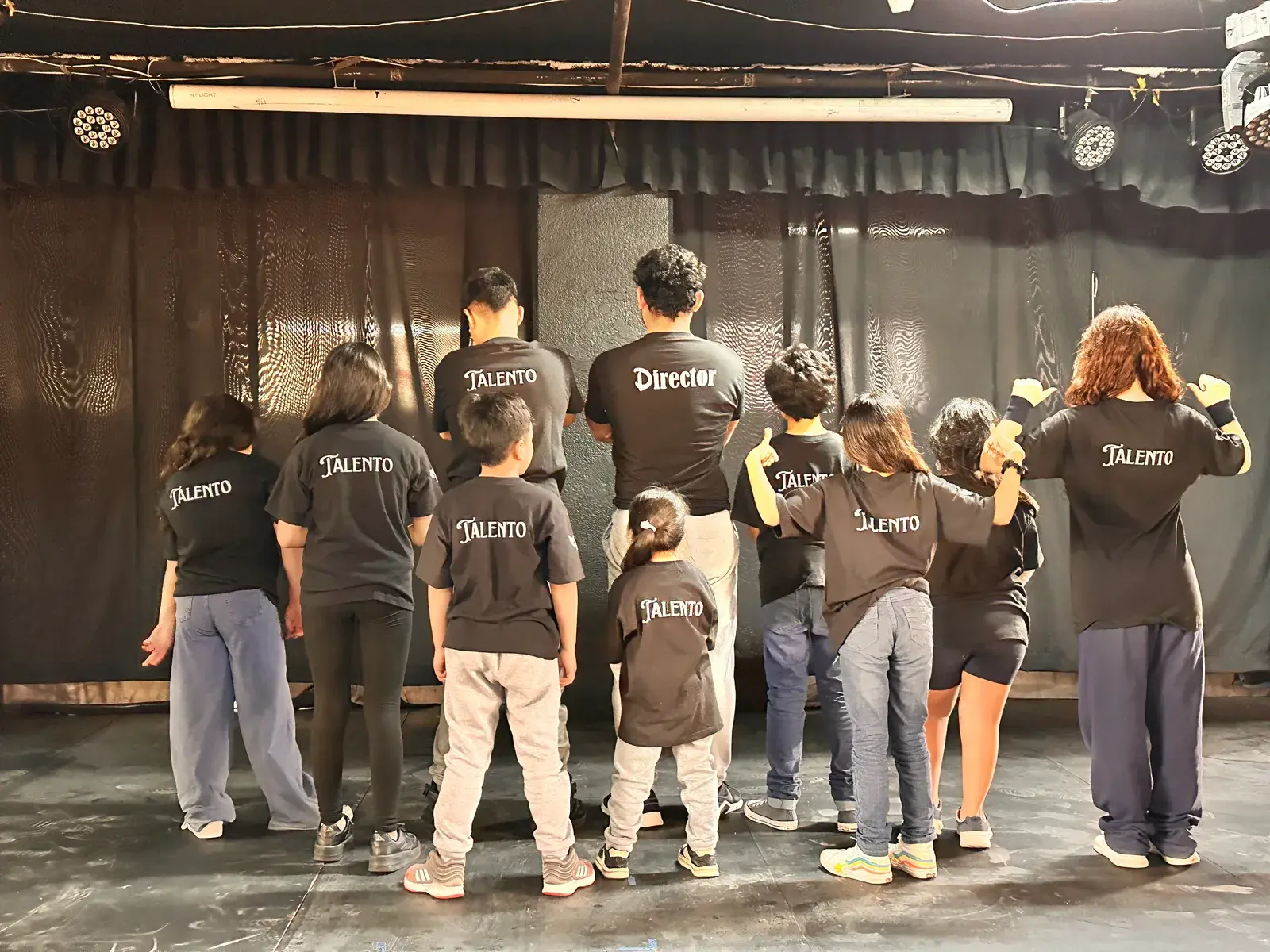 Estudiantes de CADE Teatro con playeras de talento frente al escenario