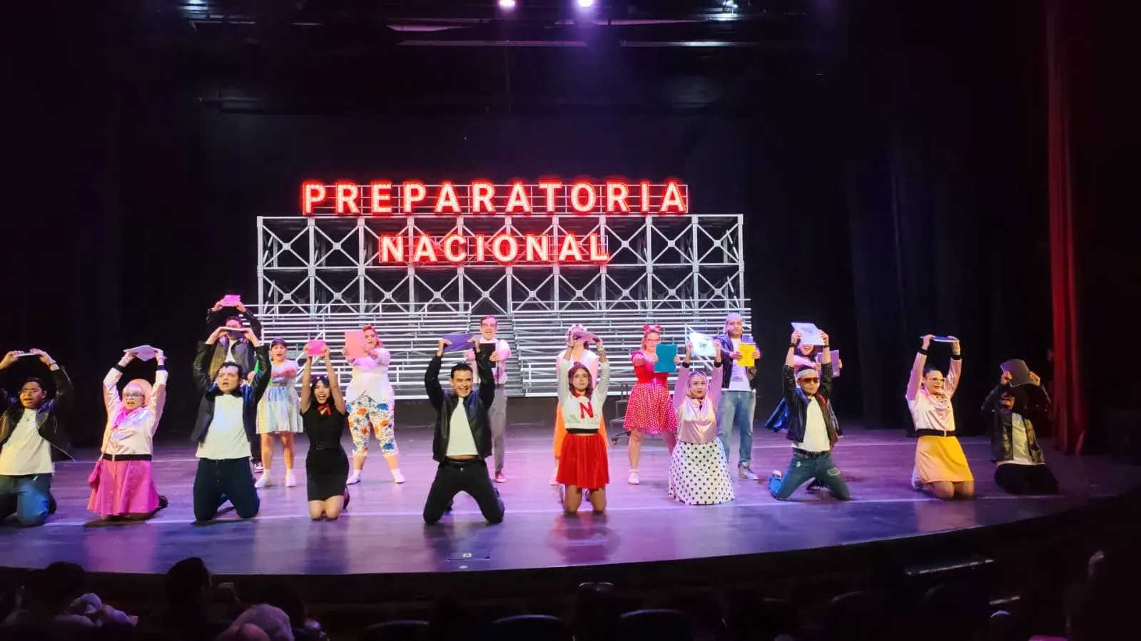 Elenco completo en el número final de una obra con letrero neón
